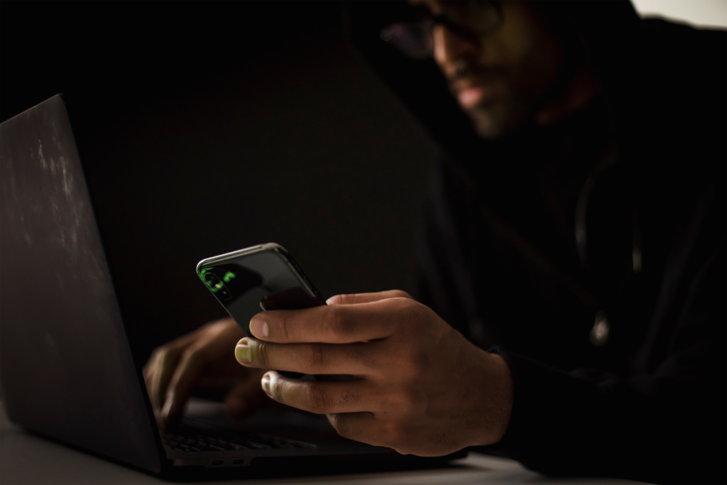 Hacker working on a laptop and holding cell phone