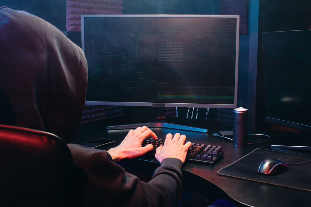 Hacker wearing a hood and working on a desktop computer