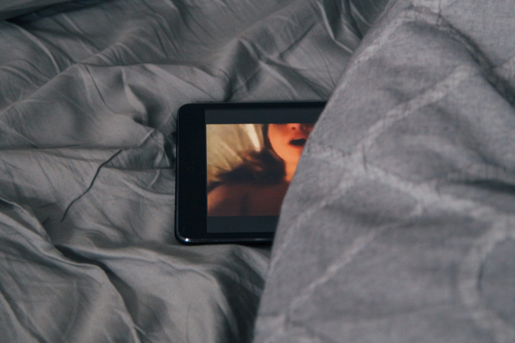 image of a tablet or phone hiding under covers while displaying pornography on the screen