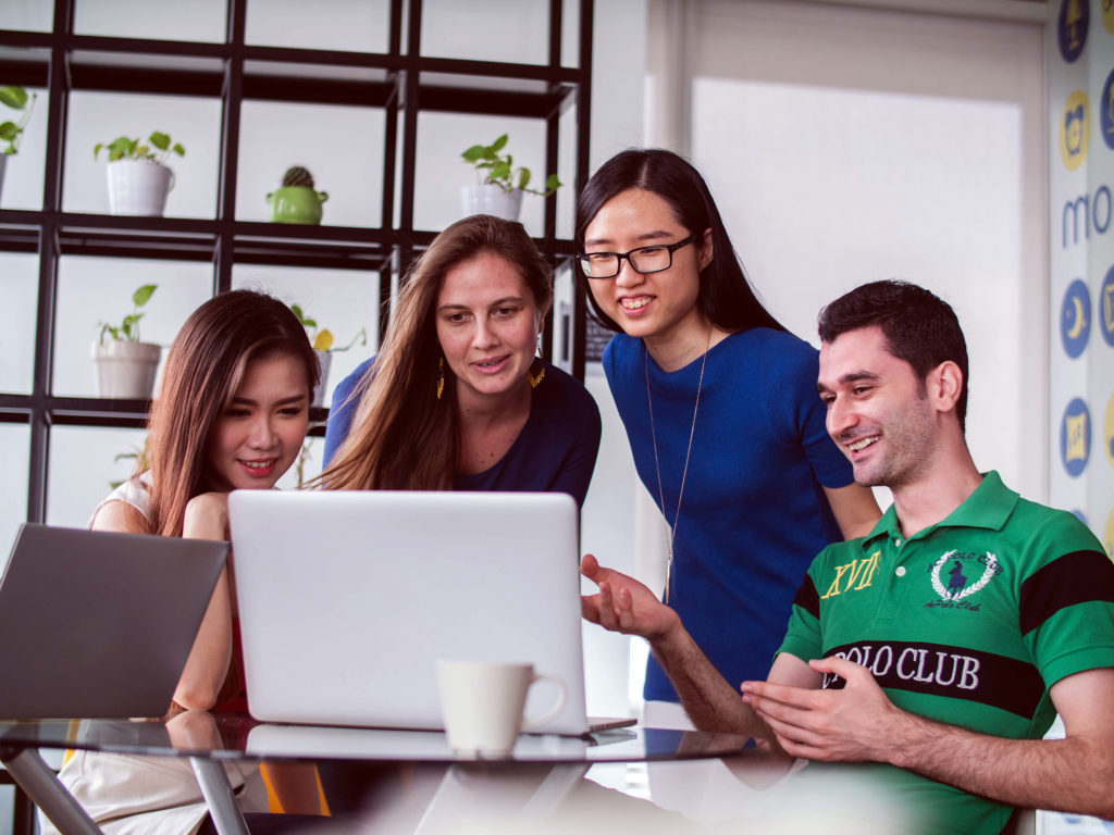 photo of a group of four people looking at a laptop screen together