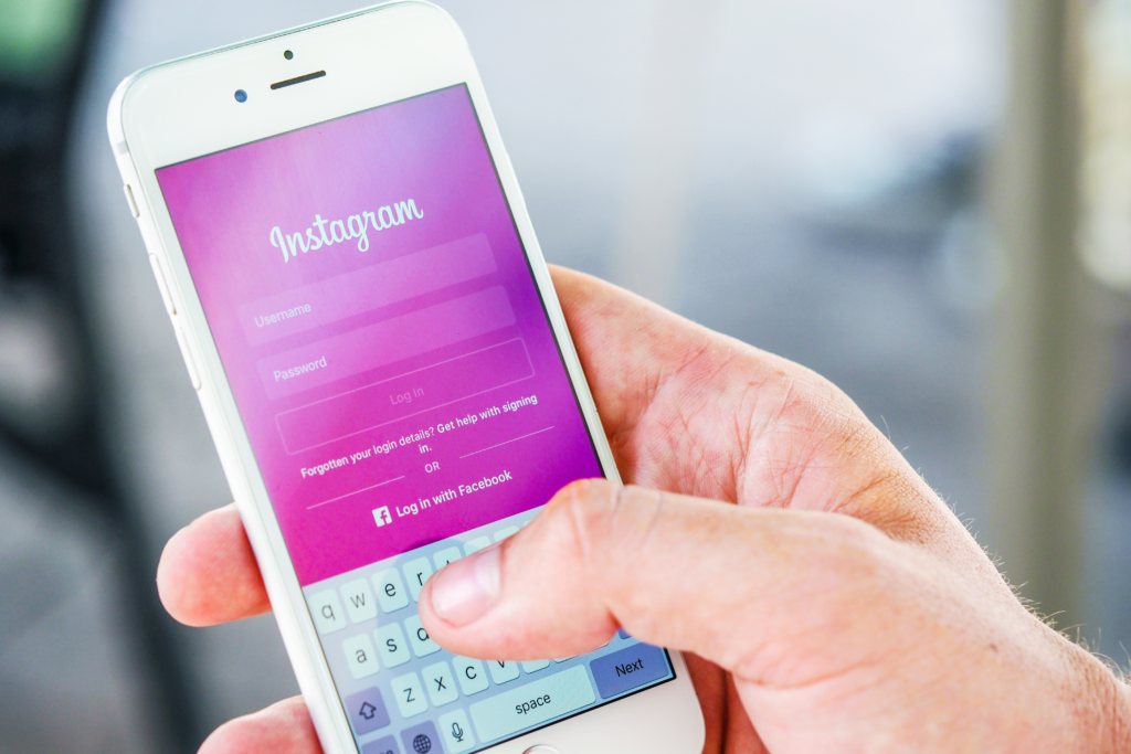 Photograph of a man's hand holding an iPhone with the Instagram login screen visible