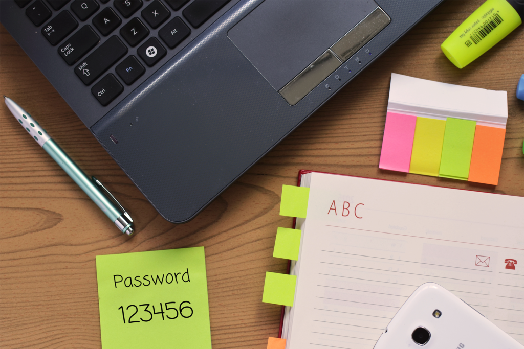 Photograph of a laptop computer surrounded by office supplies with a password written on a Post-It note